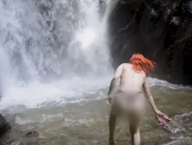 Sie zieht sich am Wasserfall im Freien aus